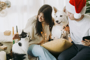 Happy young family sitting with cute dog and cat in festive decorated boho room. Merry Christmas!