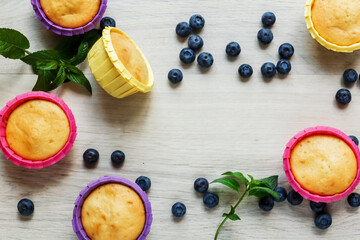 Muffins in multi-colored paper tins and blueberries on a light wooden background. Sweet pastries. Homemade baking. Sweets for the holiday. Freshly baked cupcakes on a wooden background.