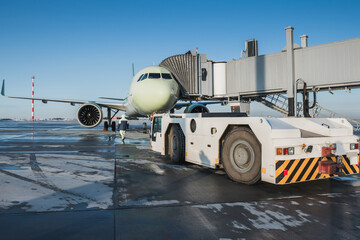 The tow tractor approaches the passenger airplane at the boarding bridge