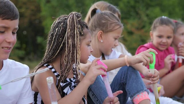Group of happy kids blow soap bubbles in summer park