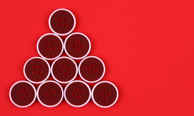 A small Christmas tree made of red buttons on a red background. Christmas, new year, minimalism