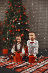 Kids sitting near Christmas tree. Children open boxes with gifts.
