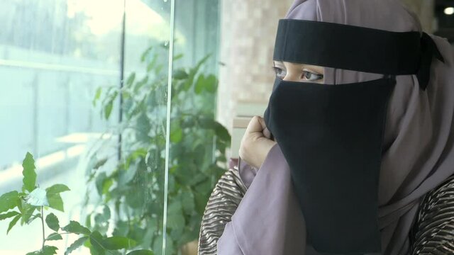 young muslim women covering face looking through window indoor