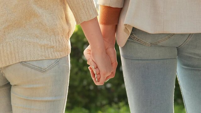 Close-up of hands joining together with sunlight flare in the background. Beautiful romantic moment between two lesbian lovers. Female couple holding hands. LGBT Pride Month, Gay Pride Symbol