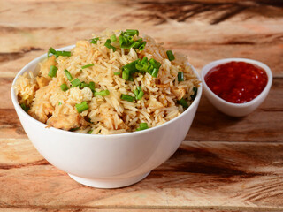 Indian cuisine Healthy and tasty chicken fried rice with tomato sauce served in white bowl over a rustic wooden background, selective focus