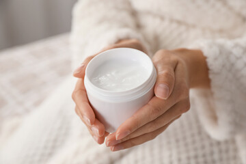 Woman with jar of moisturizing cream indoors, closeup