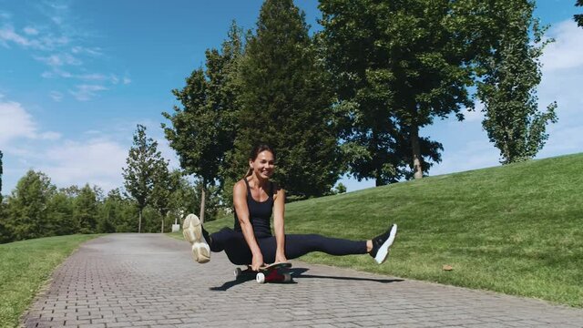 Beautiful fitness girl rides while sitting on a skateboard down.In an open Park