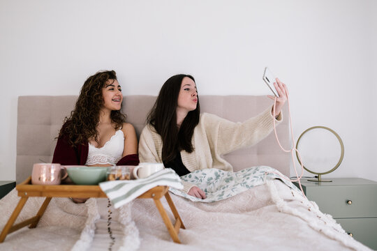 Two white teenage girls taking a selfie in bed in the morning before breakfast