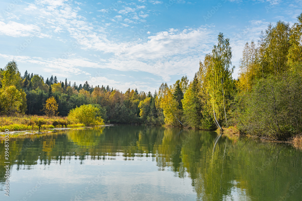Wall mural autumn forest trees are reflected in the river water of the panoramic landscape. blue sky with cloud
