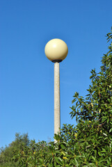 Isolated Street Lamp with Concrete Post and White Glass Globe against Blue Sky and Trees