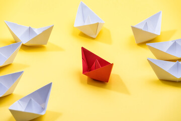 Circle of paper boats, and red colored one standing out from the crowd, leadership and individuality concepts