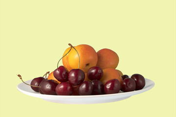 ripe delicious apricots and cherries on a light plate on a colored background