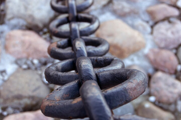 Old forged rusty chain with peeling paint on the background of paving stones.