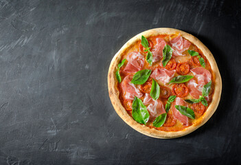 Top view to Italian pizza with prosciutto, tomato, mozzarella on a black board with copy space