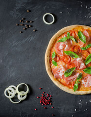 Top view to Italian pizza with prosciutto, tomato, onion, mozzarella, basil and ingridients on a black background
