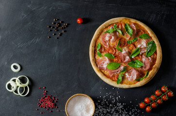 Top view to Italian pizza with prosciutto, tomato, onion, mozzarella and ingridients on a black background