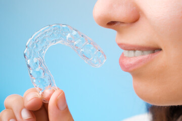 Close up woman holding a transparent removable braces for perfect smile on the blue background. Orthodontic aligners for straightening and whitening teeth. © vladim_ka