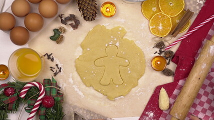 Fototapeta na wymiar A young woman makes a traditional festive Christmas cookie in the form of a human. A figuru is placed in the dough. View from above.