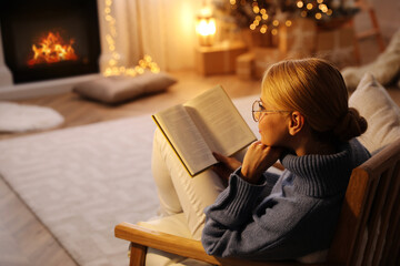 Young woman reading book at home, space for text. Christmas celebration