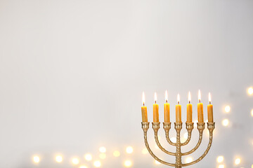 Golden menorah with burning candles against light grey background and blurred festive lights, space for text