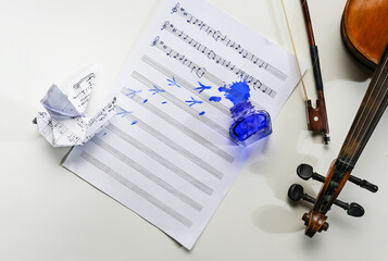 Sheet of music with a handwritten folk song, overturned ink jar and an origami dove, violin and bow...