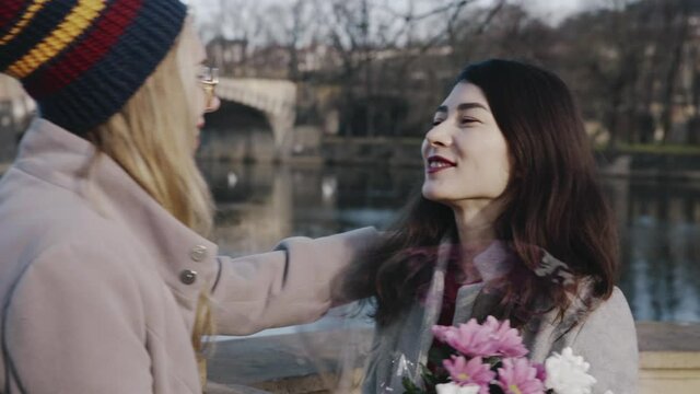 Close-up portrait of happy lesbians on date. Blonde girl giving asian girlfriend bunch of flowers. Young homosexual couple spending time together on holiday of valentine day. Romantic, LGBTQ concept.