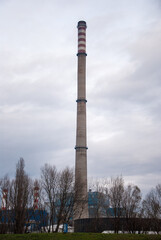 High factory chimney heating plant against the grey cloudy sky