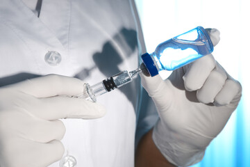 Doctor filling syringe with vaccine from vial on light background, closeup