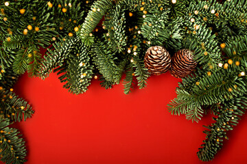 Festive red horizontal background with border from Christmas tree branches and cones.Bright bokeh lights on them. Copy space for text,new year natural layout.