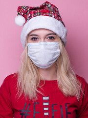 Young woman with medical mask and santa hat on pink  background. Christmas on quarantine. mask safe from coronavirus covid-19 isolated . Happy New Year celebration  merry holiday concept. panorama. 