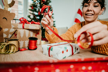 Woman sitting in her living room wrapping and decorating gifts for christmas. Christmas time