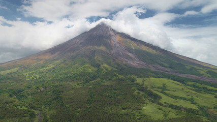 Fototapeta na wymiar Aerial of volcano peak eruption clouds of haze. Hiking path at hillside green grass valley. Philippines countryside tourist attraction of Mayon Mount, Legazpi town. Nobody nature landscape at summer