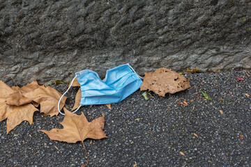 Carelessly discarded blue face mask on a sidewalk during the corona pandemic, when people are...