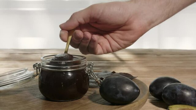 Man eating tasty plum jam from jar on table