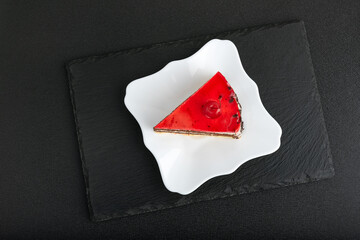 Piece of red fruit cake on white plate. Top view of cake on black background