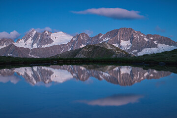 Alpine peaks reflected in mountain lake during blu hour, Stelvio National Park, Lombardia, Italy