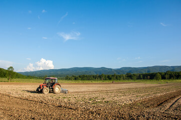 Farming with tractor and plow in field with mountain Papuk in the background, Croatia