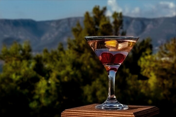 Glass with martinis, with lemon slices and cherries, on a wooden surface, isolated against the background of the nature of Turkey. Beautiful background with space for copying text.