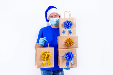 Safe contactless remote delivery of holiday gifts during coronavirus. A courier in blue uniform and protective medical mask, gloves and hat Santa Claus holds large order, many gift boxes and bags