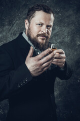 Solid bearded man in suit tasting whisky in a glass