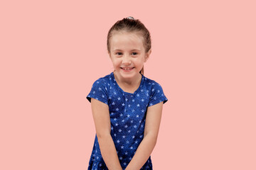 Beautiful happy girl smiles and looks at the camera. In a blue dress with a small star print. Pink isolated background.