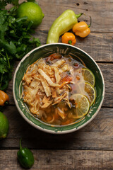 Mexican lime soup with chicken on wooden background