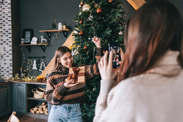 Two cheerful caucasian women friends having fun and making photo with gifts and Christmas tree.