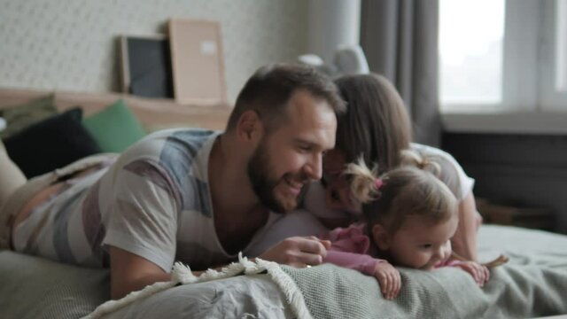 Affectionate family cute adorable funny little kid daughter embrace kiss dad and mom lying relaxing on bed, happy loving parents and child girl enjoy bonding hugging having fun playing in bedroom