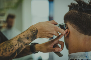 a young man with tattooed arms cuts a man's hair in a barbershop