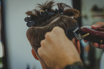 detail of a young man with tattooed arms cuts a man's hair in a barber shop