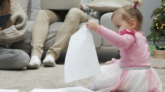 Cute little baby girl drawing pictures playing by herself on Christmas Eve while parents working. Independent kid. Careless childhood. Happy young caucasian family having fun in living room at home