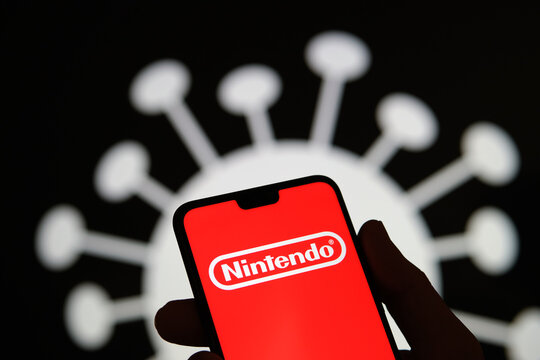 Nintendo company logo on a smartphone silhouette hold in hand. Coronavirus image on the blurred background. Real photo, not a montage.