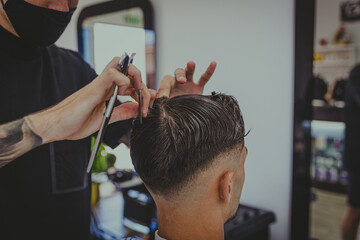 detail of a young man with tattooed arms cuts a man's hair in a barber shop