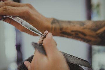 detail of a young man with tattooed arms cuts a man's hair in a barber shop